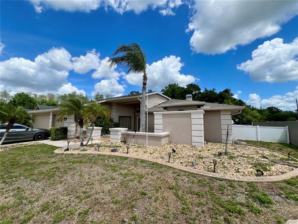 A single-story house with a beige exterior, a palm tree, and a rock-covered front yard — 5810 REDHAWK DRIVE, NEW PORT RICHEY, FL