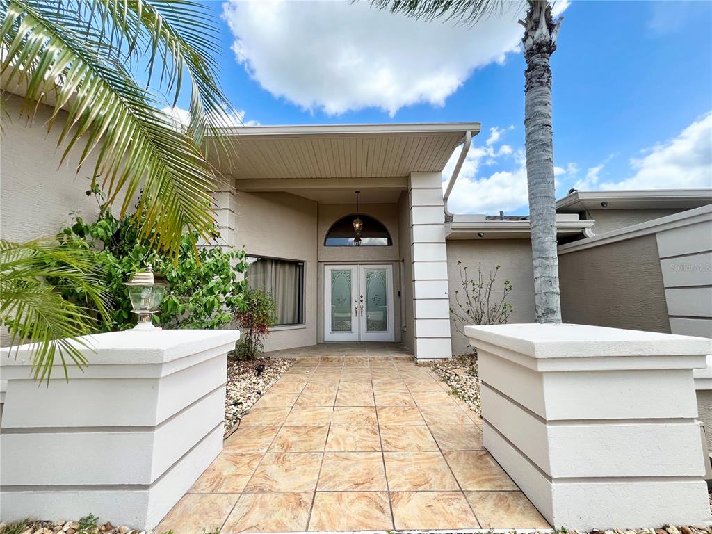 A tiled walkway leads to the double front doors of a beige stucco house — 5810 REDHAWK DRIVE, NEW PORT RICHEY, FL