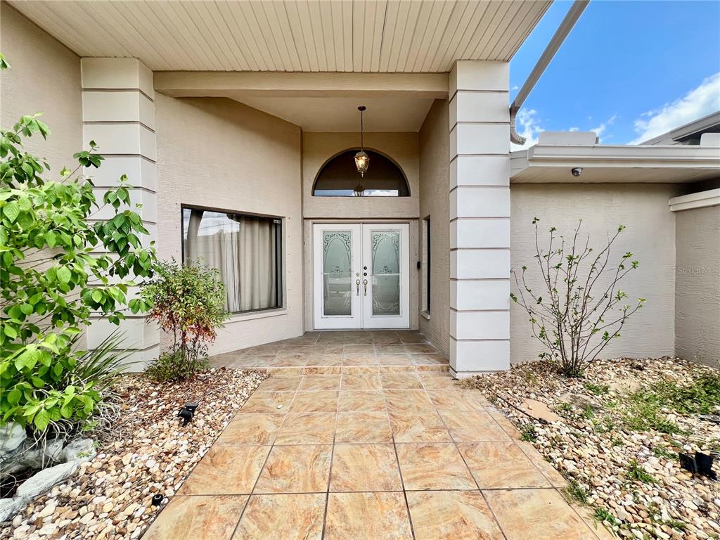 The exterior entrance features a tiled walkway leading to double glass doors under a portico — 5810 REDHAWK DRIVE, NEW PORT RICHEY, FL