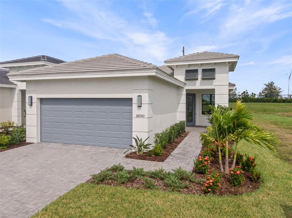 A single-story house with a gray garage door, white stucco exterior, and a paved walkway — 18340 ROCKPORT PLACE, LAKEWOOD RANCH, FL