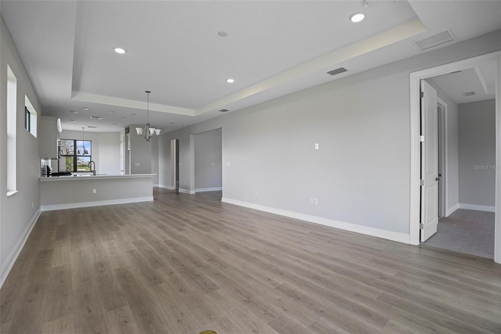 An open-concept living area features light gray walls, wood-look flooring, and a tray ceiling — 18340 ROCKPORT PLACE, LAKEWOOD RANCH, FL