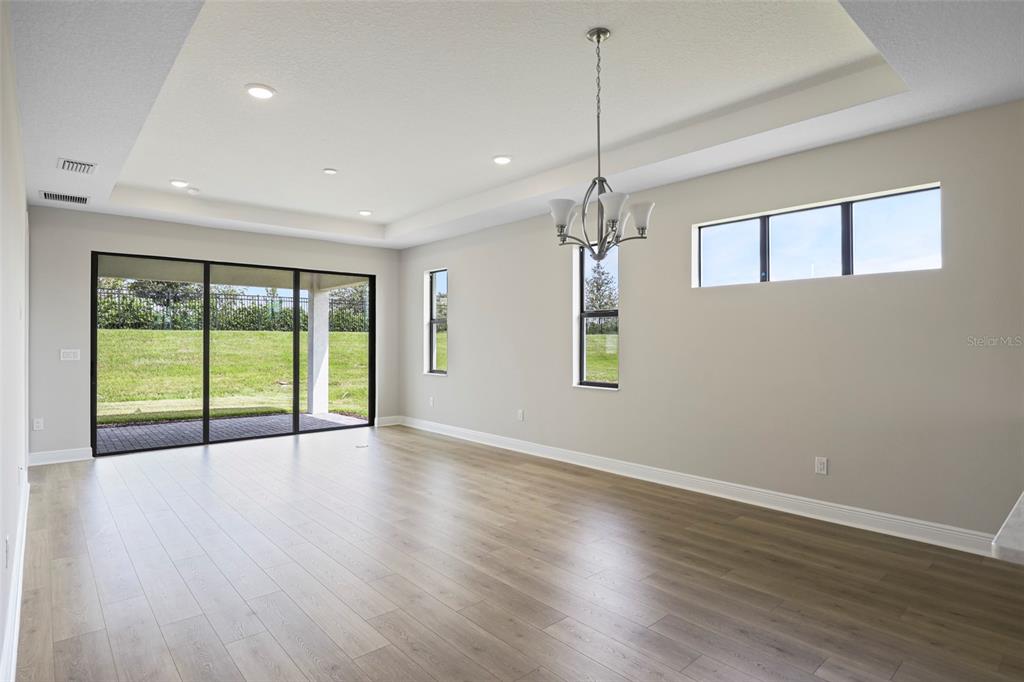 A bright, empty living room with light wood floors, a tray ceiling, and sliding glass doors — 18340 ROCKPORT PLACE, LAKEWOOD RANCH, FL