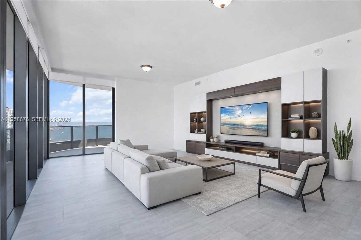 A modern living room features a large sectional sofa, a media console, and floor-to-ceiling windows — 1000 Brickell Plz, Miami FL 33131, MIAMI, FL
