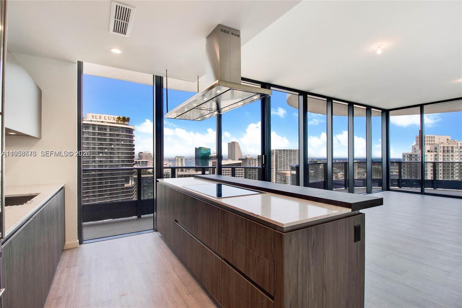 A modern kitchen features a dark wood island with a cooktop and floor-to-ceiling windows — 1000 Brickell Plz, Miami FL 33131, MIAMI, FL