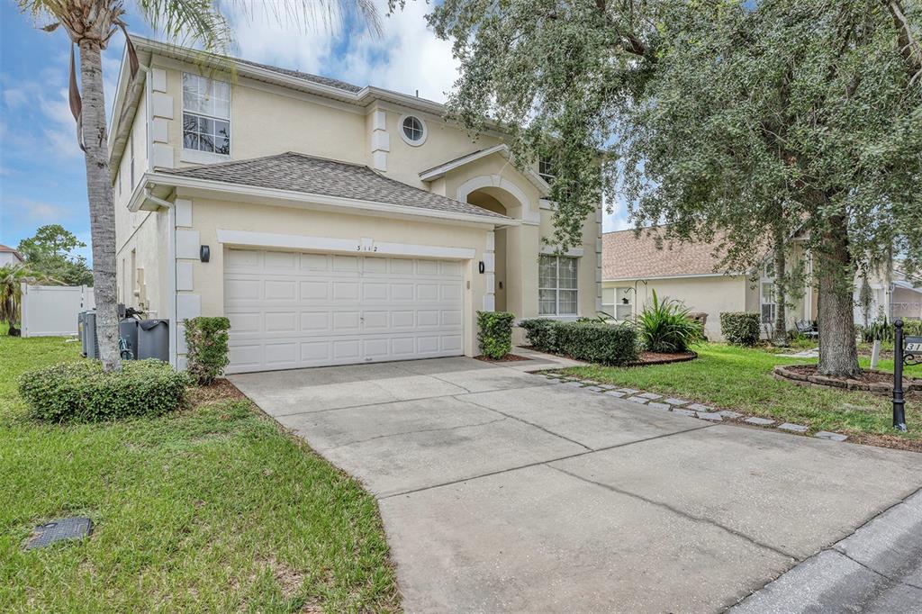 A two-story suburban house with a beige stucco exterior, a two-car garage, and a driveway — 3112 ANTIQUA WAY, HAINES CITY, FL