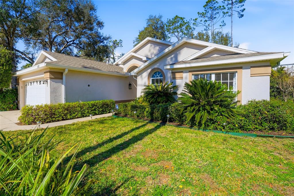 A single-story house with a beige exterior, a two-car garage, and a landscaped front yard — 5712 WHITEBARK DRIVE, WESLEY CHAPEL, FL