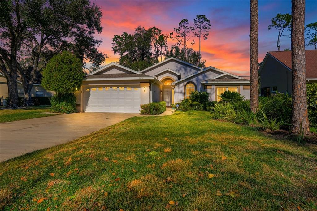 A single-story house with a two-car garage and a lawn at sunset — 5712 WHITEBARK DRIVE, WESLEY CHAPEL, FL