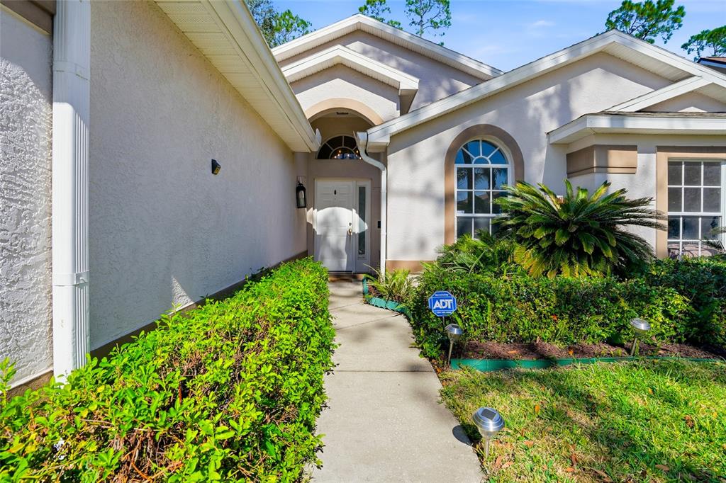 A concrete walkway leads to the front entrance of a house with beige stucco siding — 5712 WHITEBARK DRIVE, WESLEY CHAPEL, FL