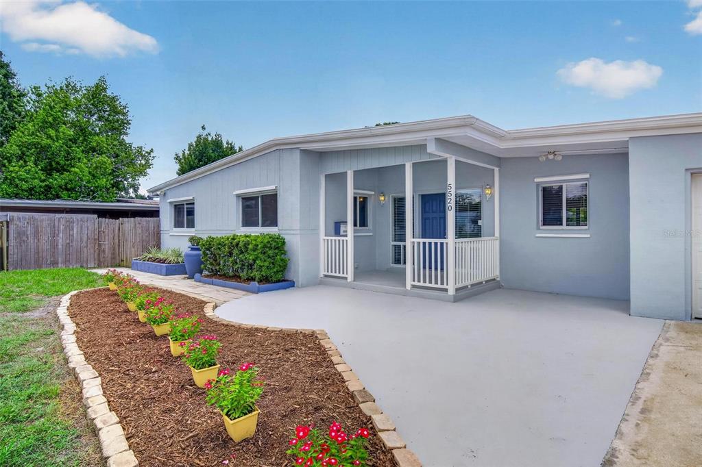 A light blue house features a covered front porch, a concrete patio, and landscaped flowerbeds — 5520 8TH AVENUE N, ST PETERSBURG, FL