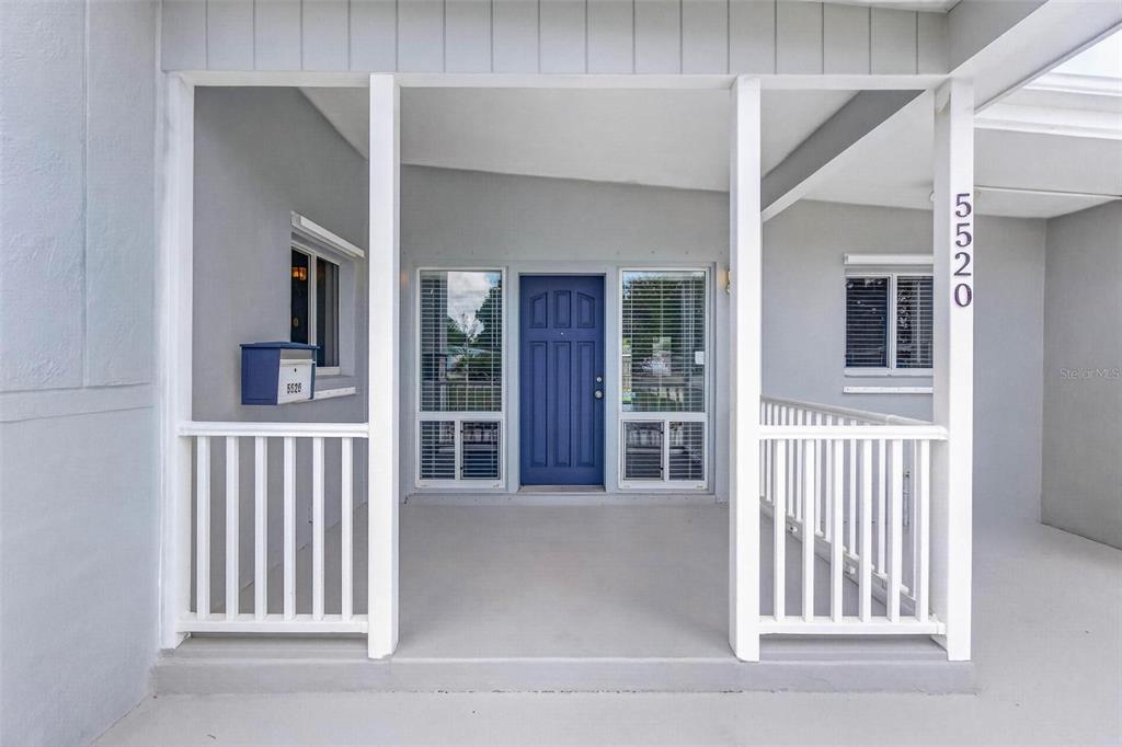 A covered porch features a blue front door, white railings, and a matching blue mailbox — 5520 8TH AVENUE N, ST PETERSBURG, FL