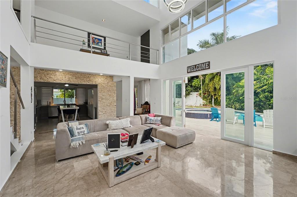A bright, open-concept living room features a large sectional sofa, stone wall, and floor-to-ceiling windows — 2A GIGI STREET, URB.SANTA MARIA, SAN JUAN, PR