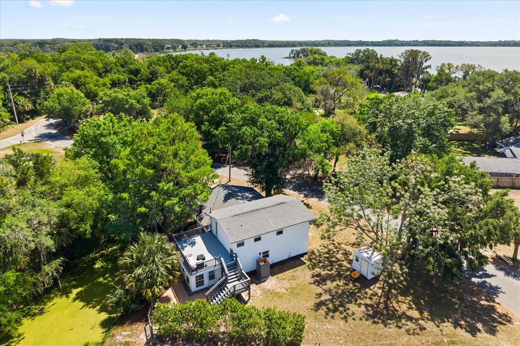 An aerial view shows a white house with a deck near a lake and trees — 7247 TREASURE ISLAND ROAD, LEESBURG, FL