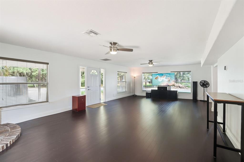 A spacious living room features dark hardwood floors, white walls, two ceiling fans, and windows — 7247 TREASURE ISLAND ROAD, LEESBURG, FL