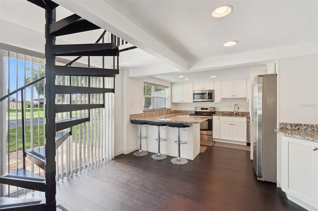 A kitchen with white cabinets, granite countertops, and a black spiral staircase near a window — 7247 TREASURE ISLAND ROAD, LEESBURG, FL
