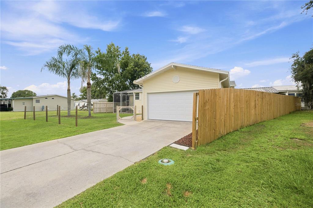 A light yellow house with a white garage door and a wooden privacy fence — 5230 LEXINGTON CIRCLE, WILDWOOD, FL