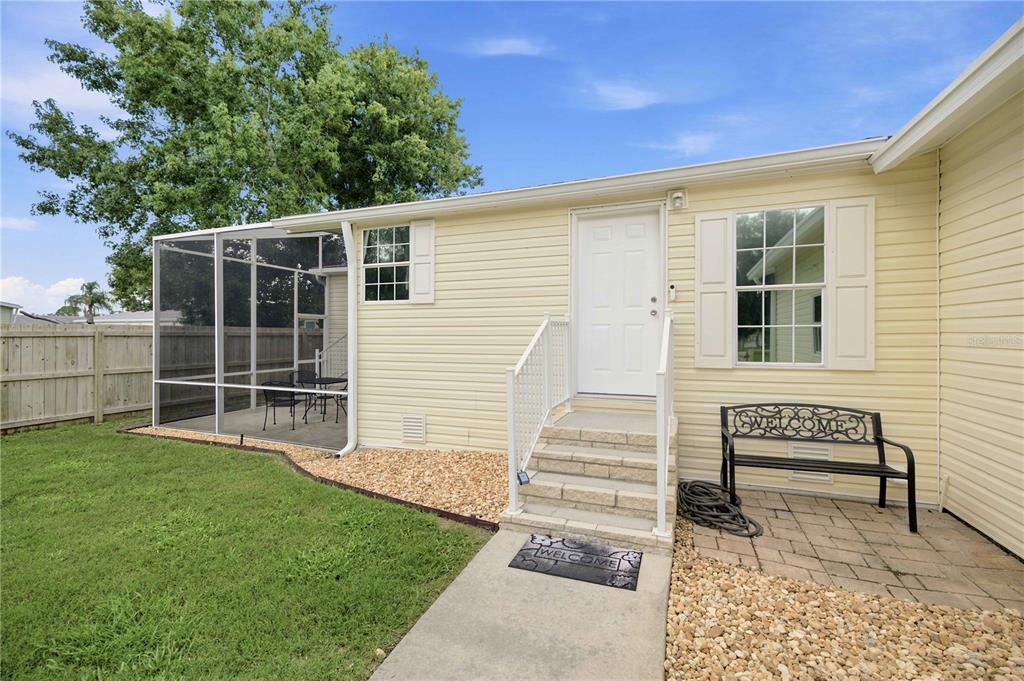 A yellow-sided house exterior features a screened-in porch, a concrete walkway, and stone steps — 5230 LEXINGTON CIRCLE, WILDWOOD, FL