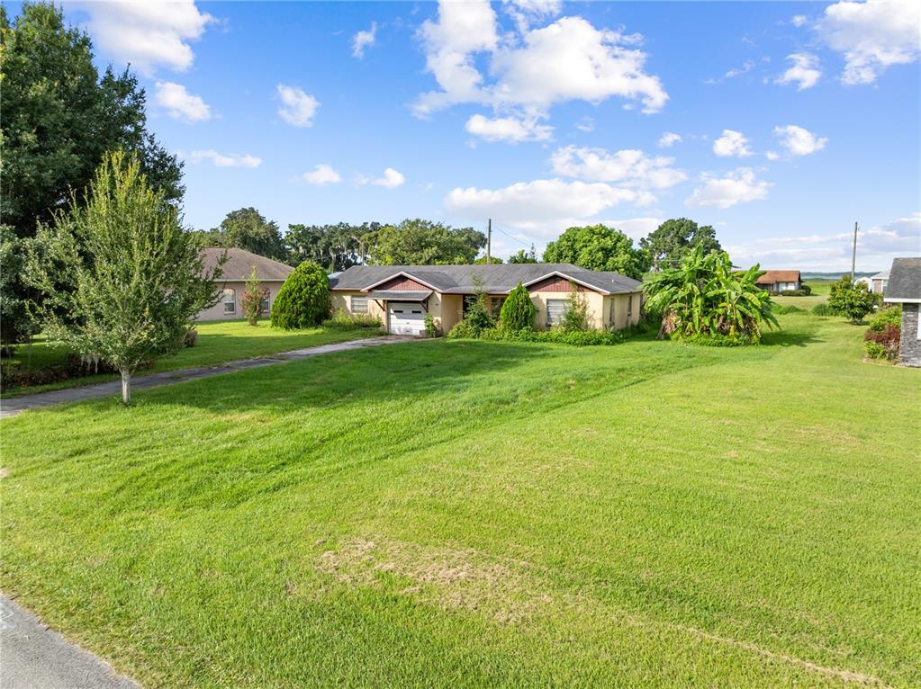 A single-story house with a garage sits on a large, grassy lot under a blue sky — 740 SHORE DRIVE, KISSIMMEE, FL