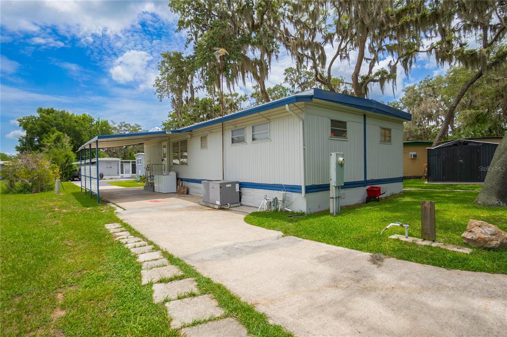 A single-story mobile home with a carport, concrete driveway, and surrounding lawn under oak trees — 3896 PICCIOLA ROAD UNIT 534, FRUITLAND PARK, FL