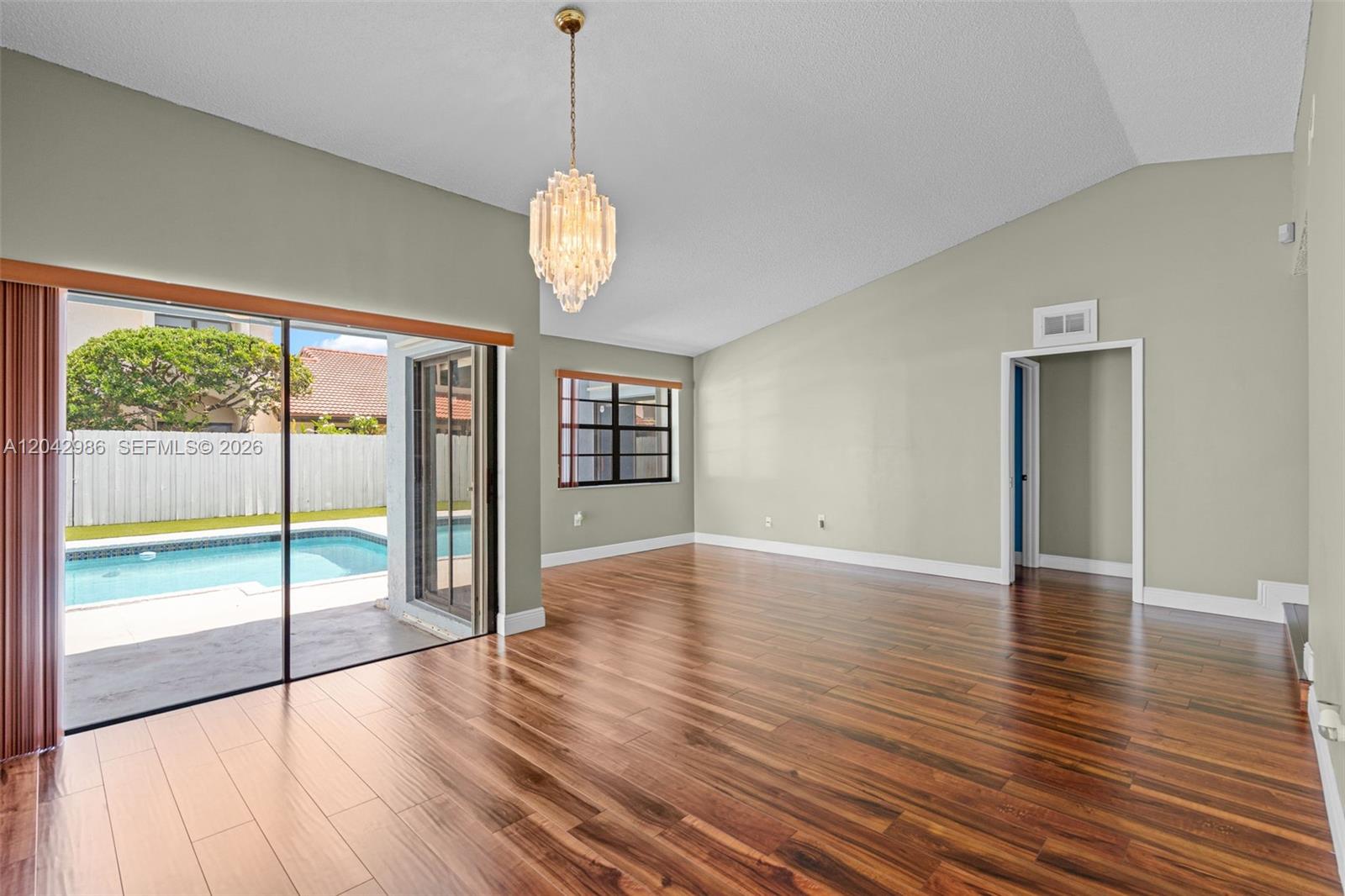 A living room with wood floors, a crystal chandelier, and sliding doors opening to a pool — 12535 SW 95th Ter, Miami FL 33186, MIAMI, FL