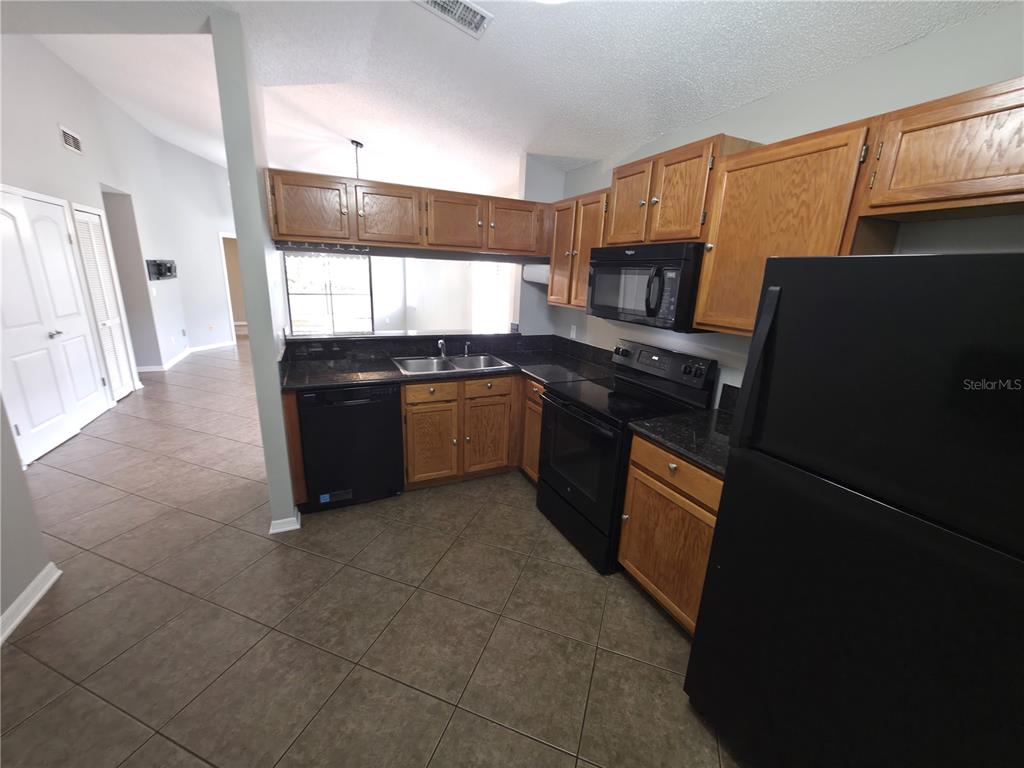 A kitchen features oak cabinets, black appliances, dark countertops, and brown tile flooring — 2201 GRASMERE DRIVE, APOPKA, FL