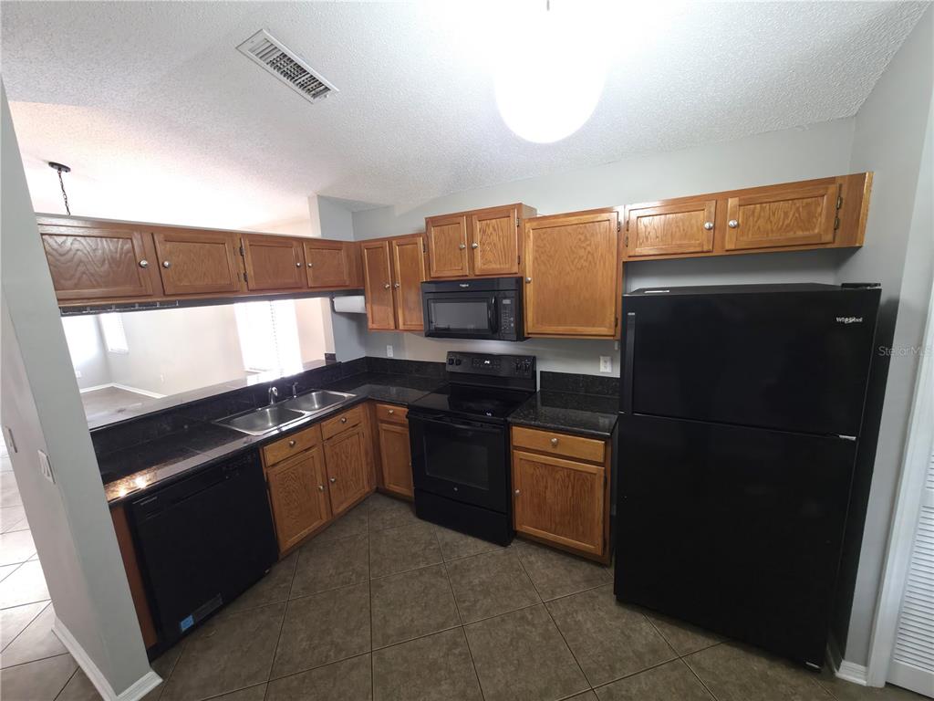 A kitchen features oak cabinets, black appliances, dark countertops, and tile flooring — 2201 GRASMERE DRIVE, APOPKA, FL
