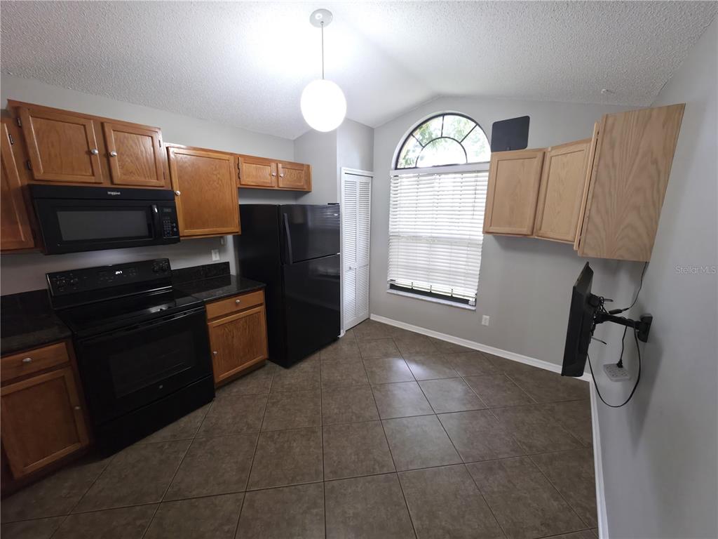 A kitchen features wood cabinets, black appliances, tile flooring, and an arched window — 2201 GRASMERE DRIVE, APOPKA, FL