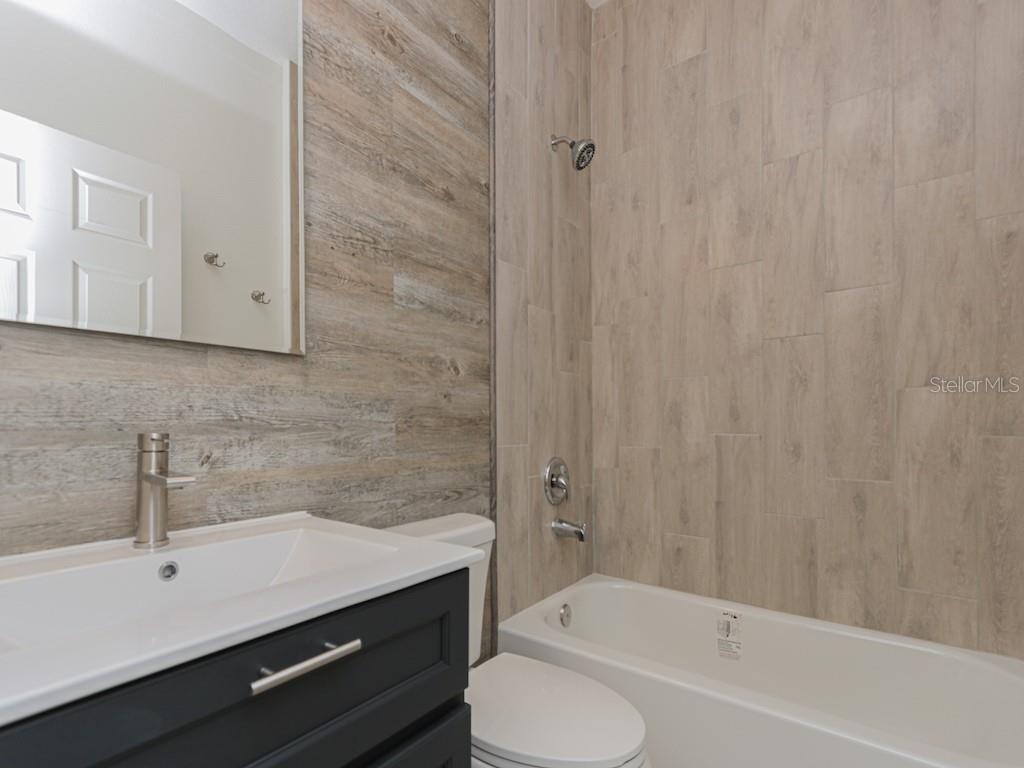 A bathroom features a dark vanity, a white sink, and wood-look tile on the walls — 2831 W LIVINGSTON STREET, ORLANDO, FL