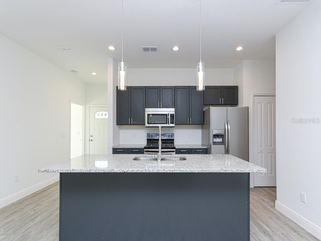A kitchen features a granite-topped island, dark cabinetry, stainless steel appliances, and light flooring — 2831 W LIVINGSTON STREET, ORLANDO, FL