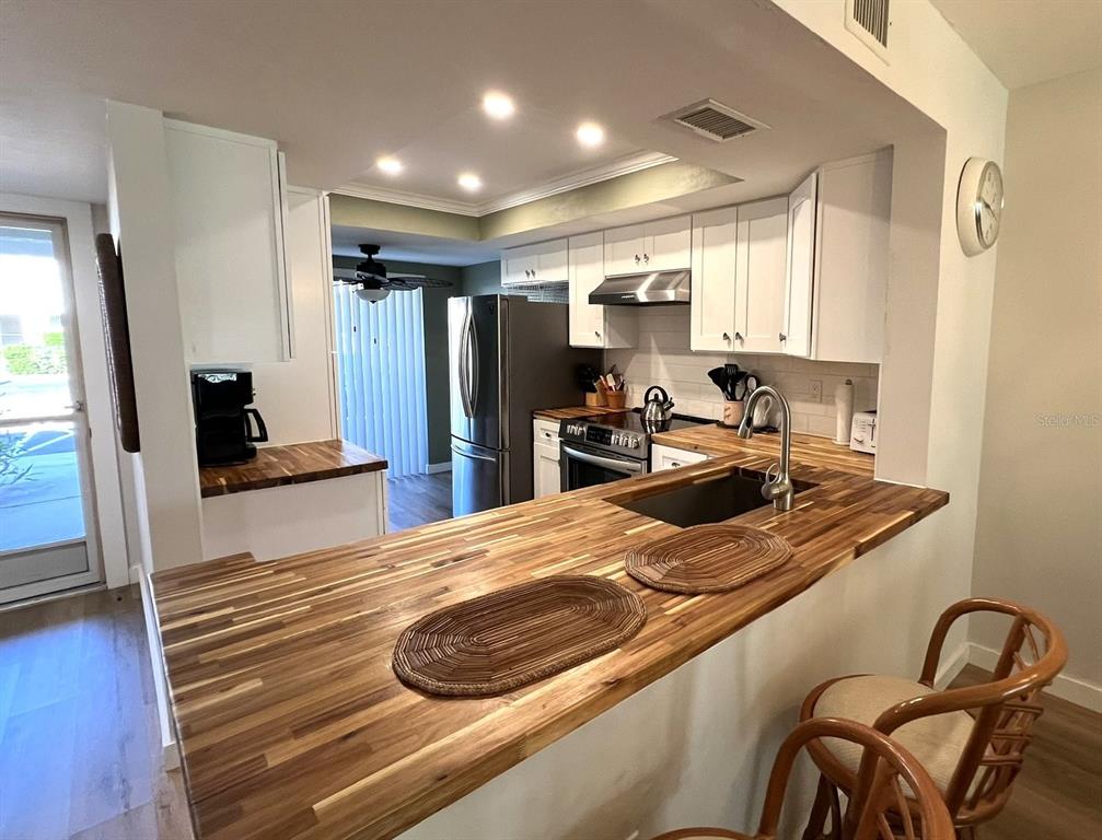 A kitchen features a wooden breakfast bar, white cabinets, stainless steel appliances, and recessed lighting — 5205 WEDGEWOOD LN UNIT 15, SARASOTA, FL