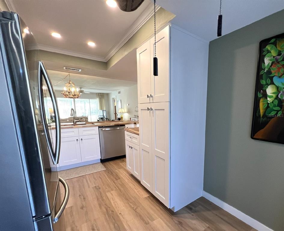 A kitchen features white cabinetry, stainless steel appliances, and light wood-look flooring — 5205 WEDGEWOOD LN UNIT 15, SARASOTA, FL