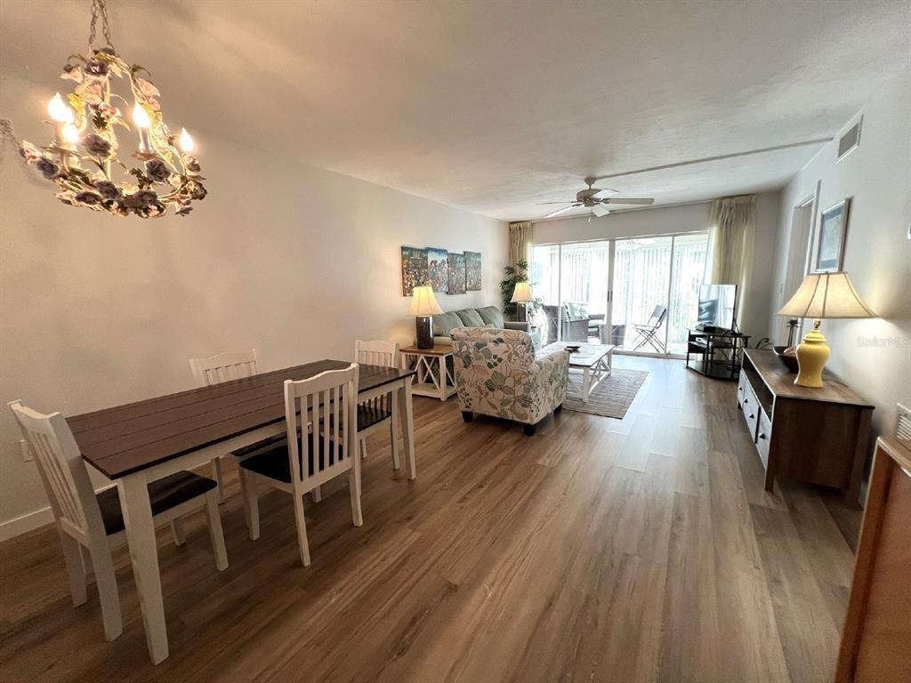 A dining area and living room with wood-look flooring, a floral chandelier, and sliding glass doors — 5205 WEDGEWOOD LN UNIT 15, SARASOTA, FL