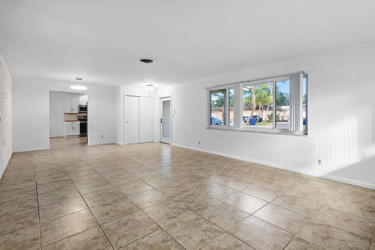 An empty living room features beige tile flooring, white walls, and a large window — 617 SE 8th Avenue, Deerfield Beach FL 33441, DEERFIELD BEACH, FL