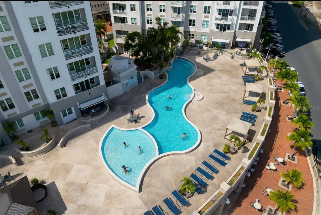 An aerial view shows a curved swimming pool surrounded by a patio and apartment buildings — 100 DEL MUELLE UNIT 1301, SAN JUAN, PR