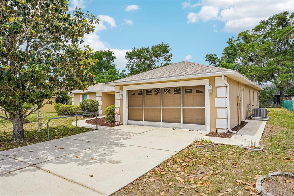 A tan single-story house with a two-car garage, concrete driveway, and a large magnolia tree — 86 BAHIA TRACE TRAIL, OCALA, FL