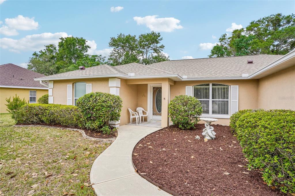 A single-story house with a beige stucco exterior, a front walkway, and landscaped bushes — 86 BAHIA TRACE TRAIL, OCALA, FL