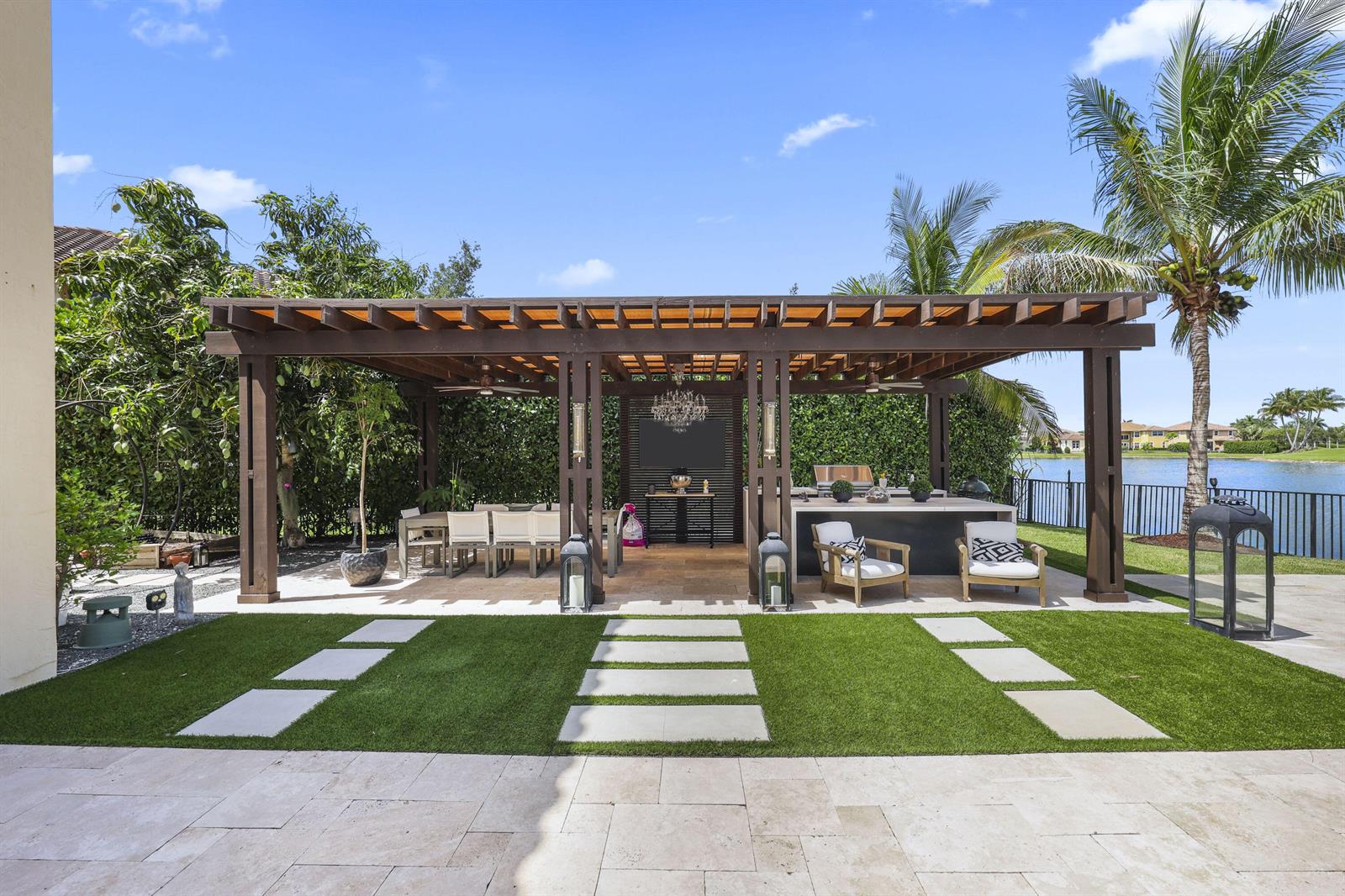 A wooden pergola covers an outdoor dining area and kitchen overlooking a lake — 8861 Edgewater Place, Parkland FL 33076, PARKLAND, FL
