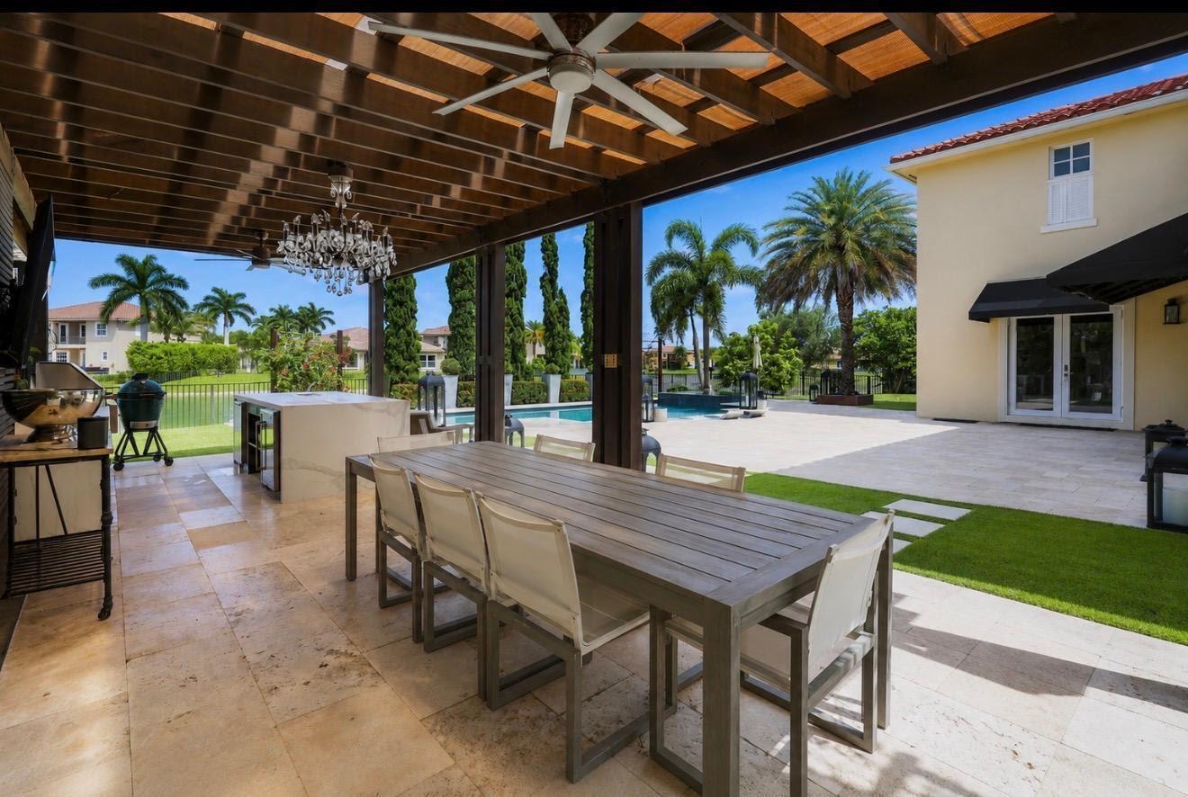 A covered outdoor patio features a dining table, kitchen island, and view of a pool — 8861 Edgewater Place, Parkland FL 33076, PARKLAND, FL