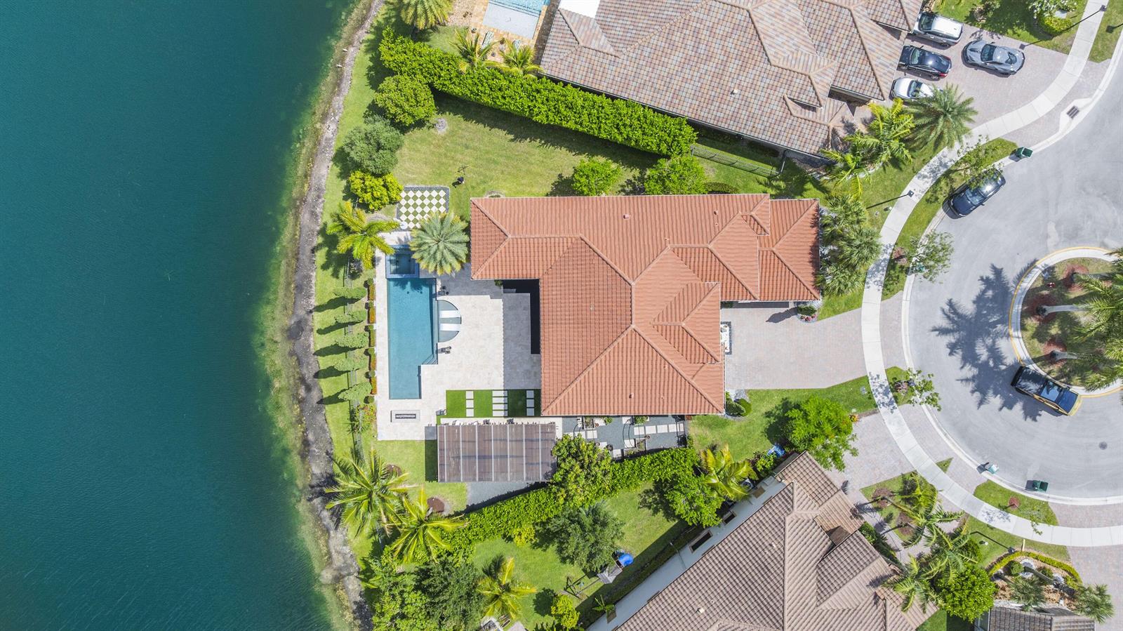 An aerial view shows a house with a tile roof, pool, and patio beside a lake — 8861 Edgewater Place, Parkland FL 33076, PARKLAND, FL