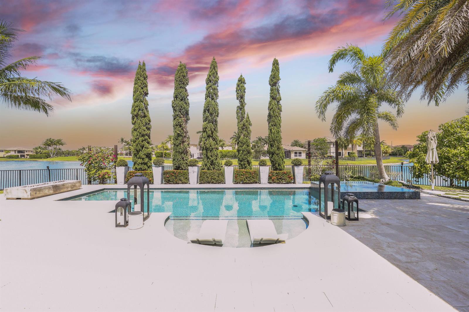 A backyard swimming pool with a tanning ledge and tall cypress trees overlooking a lake — 8861 Edgewater Place, Parkland FL 33076, PARKLAND, FL