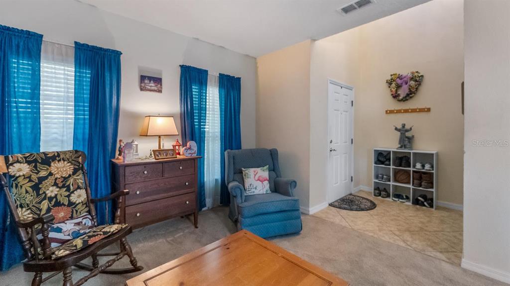 A living room features a rocking chair, blue armchair, wooden dresser, and a shoe storage unit — 219 BELLA WAY, GROVELAND, FL