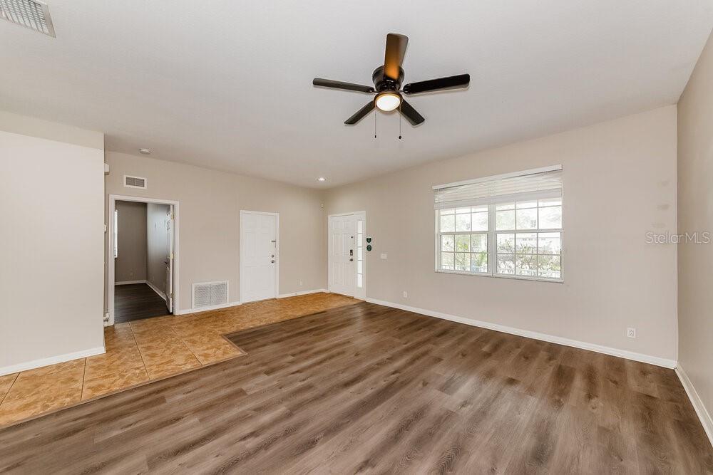 An empty living room features wood-look flooring, a ceiling fan, and a white front door — 4246 DAY BRIDGE PLACE, ELLENTON, FL