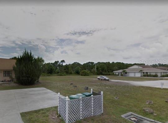 A vacant grassy lot sits between two residential buildings under a cloudy sky — 71 BOUNDARY BOULEVARD, ROTONDA WEST, FL