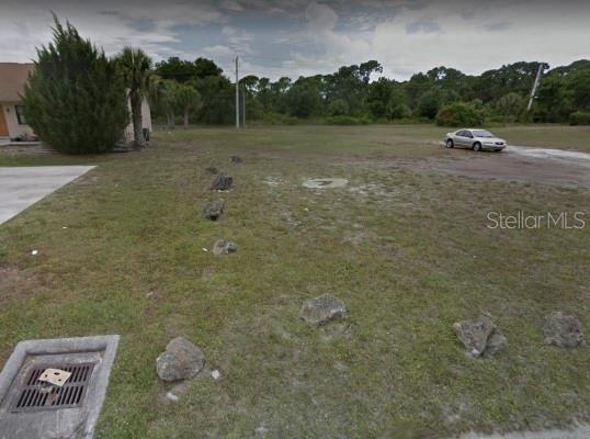 A vacant grassy lot features several decorative rocks and a storm drain in the foreground — 71 BOUNDARY BOULEVARD, ROTONDA WEST, FL