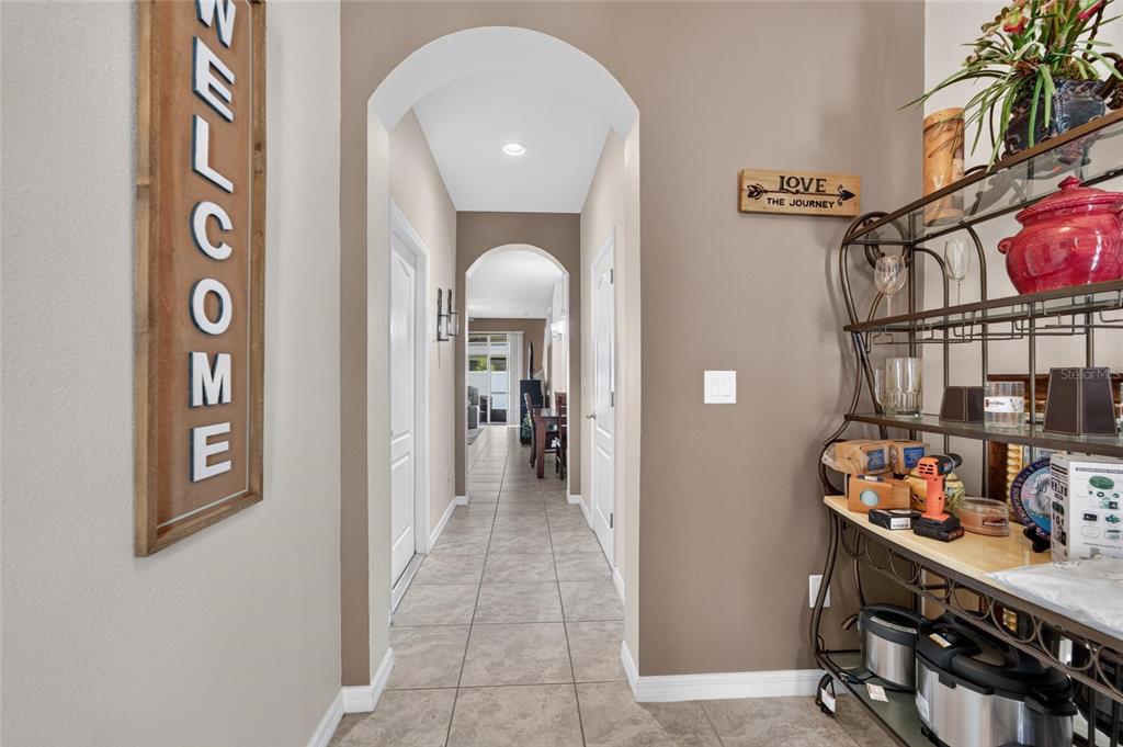 A tiled hallway with arched entryways leads toward a dining area in a home interior — 10411 RED CARPET COURT, RIVERVIEW, FL