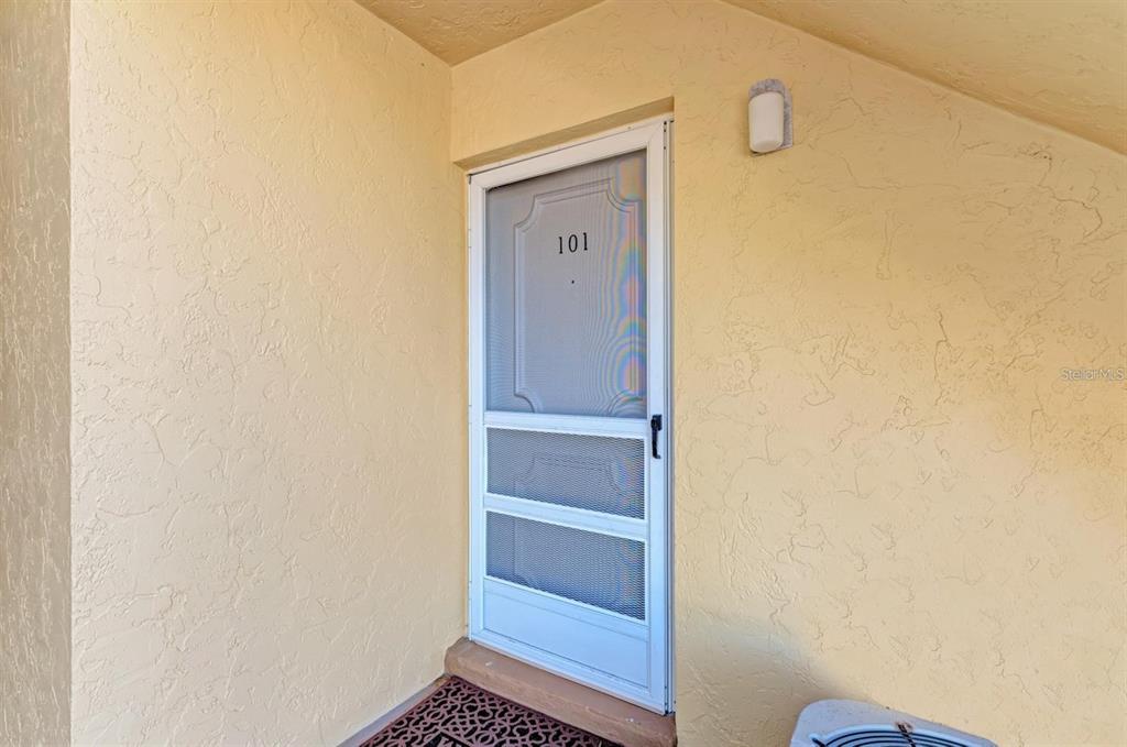 A white screen door with the number 101 is set in a light yellow stucco wall — 129 TYLER DRIVE UNIT 101, SARASOTA, FL