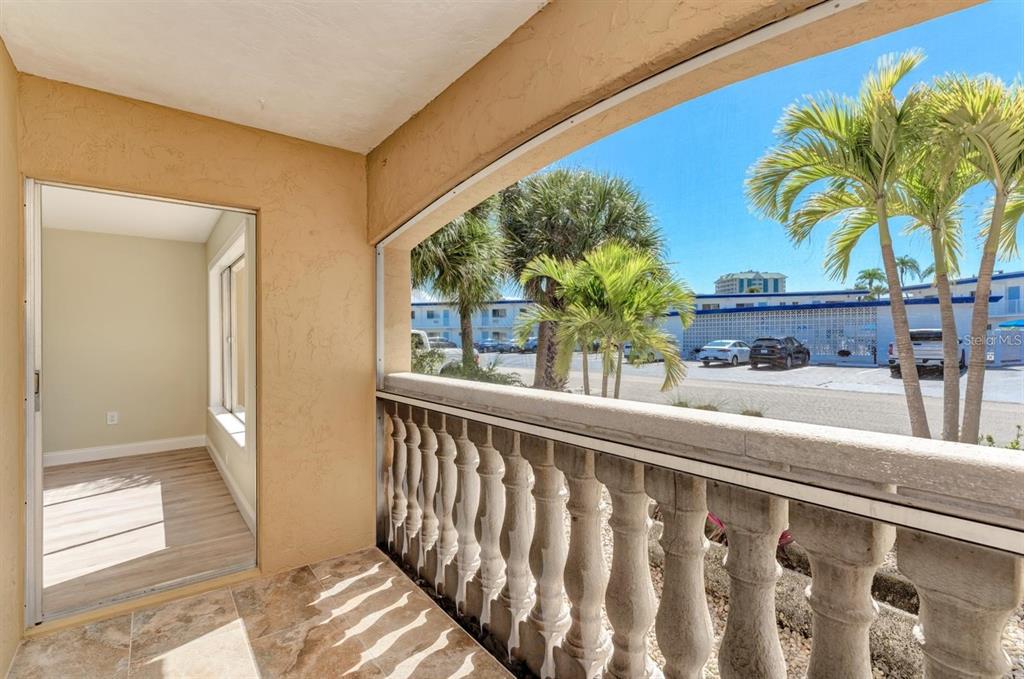 A covered balcony with a stone balustrade overlooks a parking lot with palm trees — 129 TYLER DRIVE UNIT 101, SARASOTA, FL