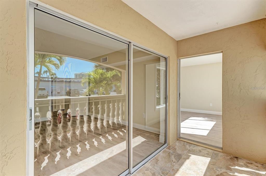 A tiled balcony with a sliding glass door looking out toward palm trees and parking — 129 TYLER DRIVE UNIT 101, SARASOTA, FL