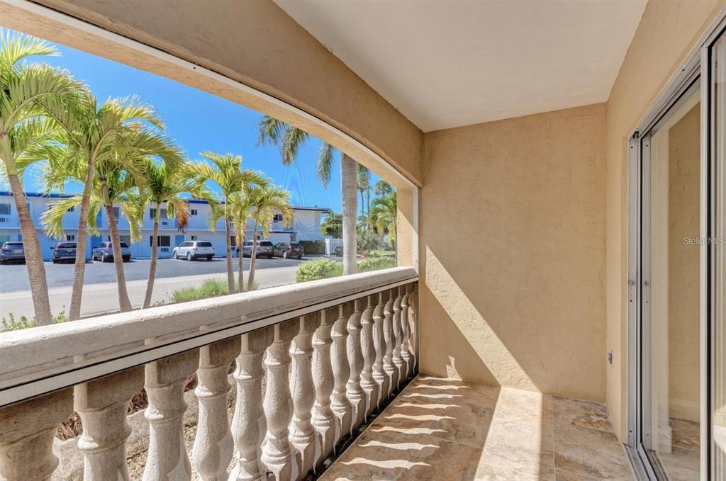 A screened balcony features a stone balustrade, tiled flooring, and views of palm trees and cars — 129 TYLER DRIVE UNIT 101, SARASOTA, FL