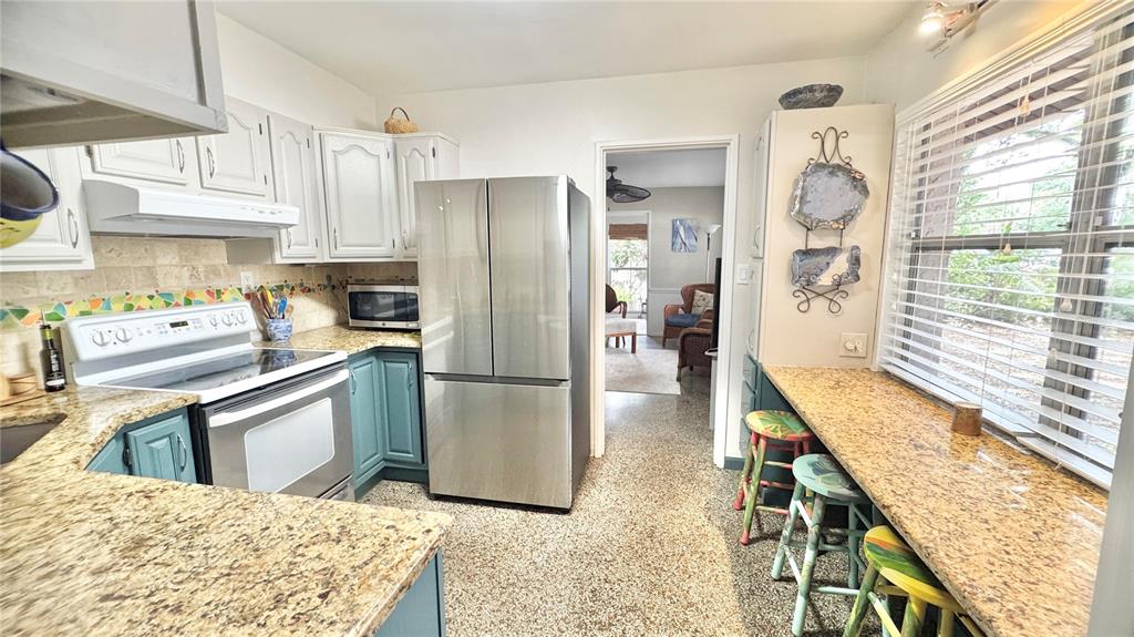 A kitchen features white upper cabinets, teal lower cabinets, granite countertops, and a stainless refrigerator — 4319 S CAMERON AVENUE, TAMPA, FL