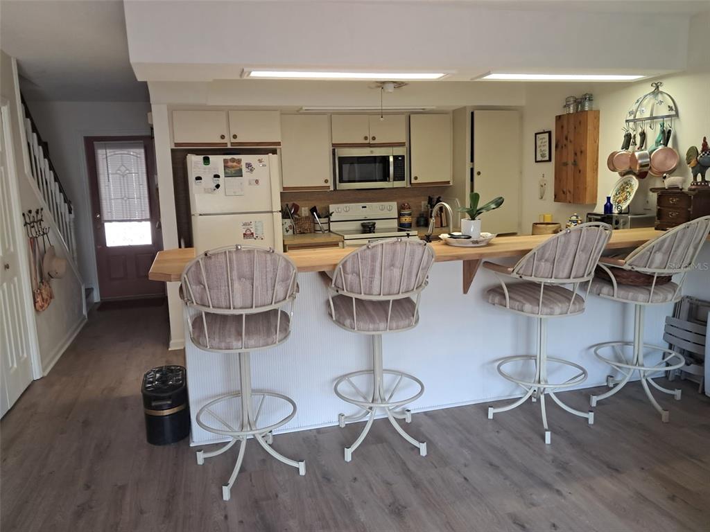 A kitchen features a breakfast bar with four stools, white cabinets, and light wood flooring — 1922 S RIVERSIDE DRIVE, EDGEWATER, FL